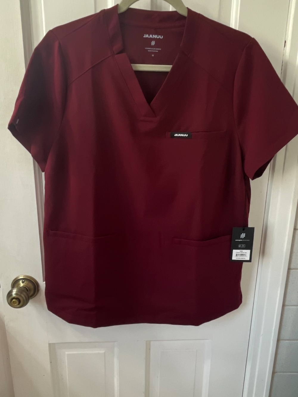 Jaanuu Women’s Helia Notched V-Neck Scrub Top in the color Burgundy. Size Medium